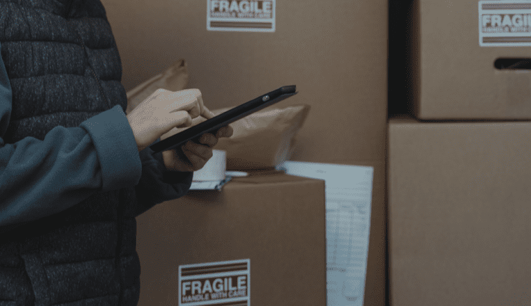 persona haciendo control de stock con una tablet y los paquetes al fondo